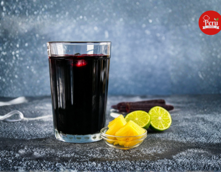 vaso de chicha morada peruana con limón verde y trozos de piña al lado sobre una mesa.